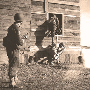 SSG Bishop Scarboro, CPL Elmer Cochran (top), and SGT Howard M. Draper (Ranger students) demonstrate how to cover a window entry of a &lsquo;Naziville&rsquo; building.