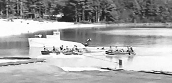 Special Forces wearing SCUBA gear jump into McKellar&rsquo;s Pond from a plywood silhouette patrol boat while an SF team paddles alongside in RB-7 rubber boats.