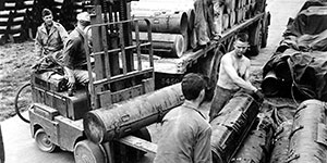 Packed containers are loaded for shipment to a local airfield. Sergeant James Gearing, on the bicycle behind the forklift, is supervising.