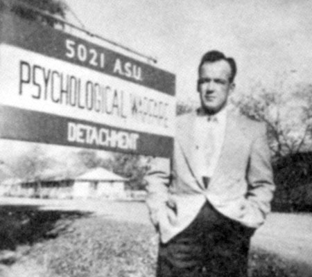 A 5021st Psychological Warfare Detachment soldier stands by the unit sign at Camp Forsyth, Fort Riley, KS.