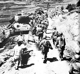 U.S. troops pass a disabled Soviet-produced T-34/85 tank. As one of the most successful tank designs in WWII, the T-34/85 outclassed American armor early in the war.