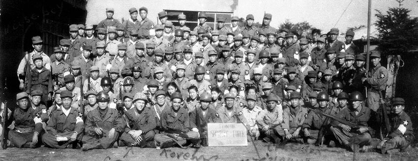 The assembled Ivanhoe Security Force with its American military cadre seated in the front row: 4th from left CPL Joseph Howard, 5th from left SGT Emmett Parker, 7th from left MAJ Jack Young, 9th from left CPL L. Carl Heesch, 12th from left CPL &ldquo;Moose&rdquo; Thompson.