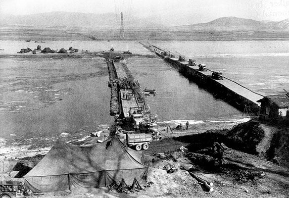 While the Highway Bridge (right) across the Taedong River had been destroyed, U.S. Army engineers quickly erected a pontoon bridge (left) to reconnect East and West P&rsquo;yongyang until the Highway Bridge could be repaired.