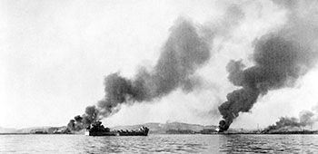 As the last troops of the 3rd Infantry Division leave Hungnam, smoke columns rise hundreds of feet into the air from the burning port facility and abandoned supplies.