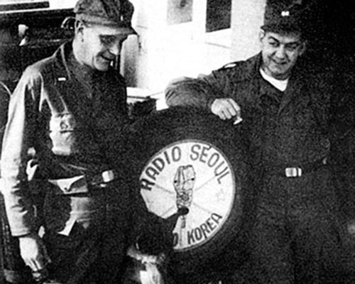 1LT Robert B. Shall, Radio Seoul, and CPT Frederick P. Laffey, 4th MRBC Radio Manager, pose with the KBS station mascot.