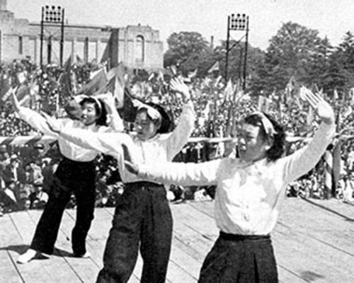 The May Day rally in Meiji Park began with entertainment by dancing girls and music. Spectators enjoyed ice cream cones and bean curd cakes while others waved festive, colorful banners.