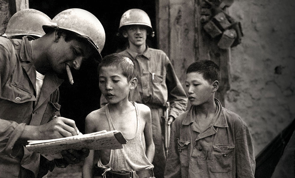 Two North Korean boys inducted into the North Korean People’s Army surrender to U.S. soldiers.