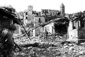 A Force combat patrol clears a ruined village near Radicosa. Private Charles N. Russell, (L) covers the advance of the patrol.