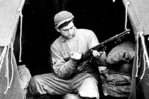 A Forceman cleans his M-1 rifle in a Bell tent on Amchitka. His knee-high shoepacs and the improvised boardwalk helped to traverse the soft muskeg of the island.